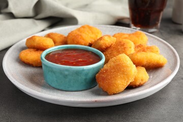 Plate with hot chili sauce and nuggets on grey textured table, closeup