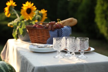 Glasses, plates, fresh products and sunflowers on table in garden, closeup