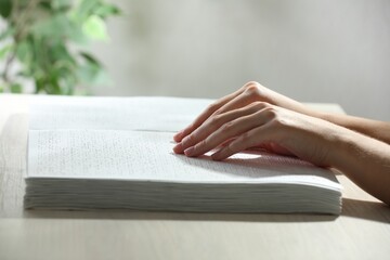 Blind woman reading book written in Braille at wooden table, closeup