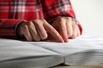 Blind woman reading book written in Braille at table, closeup