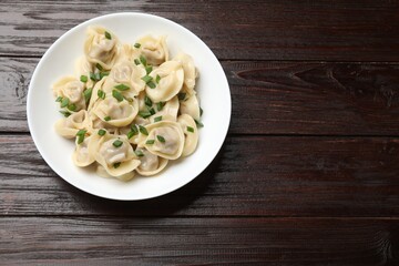 Delicious pelmeni with green onion on wooden table, top view. Space for text