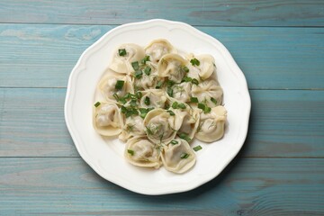 Delicious pelmeni with green onion and dill on blue wooden table, top view