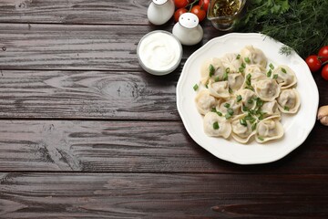 Delicious pelmeni with green onion served on wooden table, flat lay. Space for text