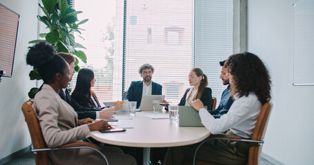 Busy director with his managers sitting at round table in modern room with panoramic window. People...