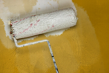 Creative graphic concept of paint roller applying fresh orange color paint onto the white concrete wall. Process of home renovation, improvement and makeover. Copy space.