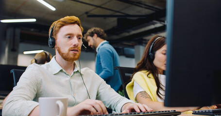 Camera view behind computer on mixed-raced workers. Busy people with headsets communicating online with customers. Call center managers answering calls and providing information. Using computers.