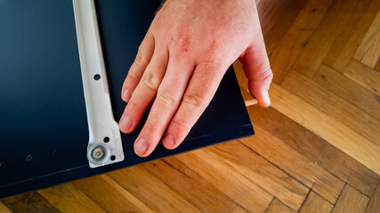 Caucasian hand installing a shelf bracket on a wooden floor; concept of home improvement and DIY projects