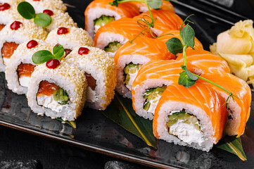Two kinds of sushi rolls with salmon and sesame seeds served on black plate