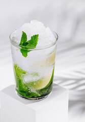 Refreshing mojito cocktail standing on white cube with tropical palm leaf shadow