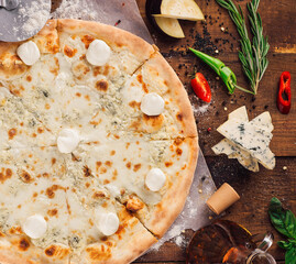 Delicious four cheese pizza lying on wooden table surrounded by fresh ingredients