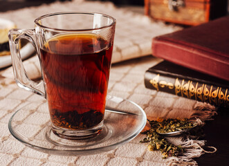 Steaming cup of tea with books and dessert on tablecloth