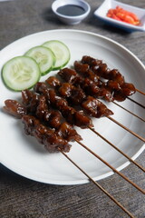 a plate satay with soy sauce and vegetables on it. Indonesian food.