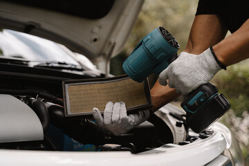 Mechanic Working on Car Air Filter: A close-up shot of a mechanic's hands, wearing white gloves, as they hold a car air filter and a power tool, suggesting maintenance or replacement.