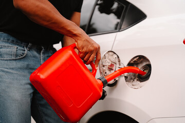 Refueling on the Go: A man carefully pours gasoline from a red gas can into his car's fuel tank.  A candid moment depicting practicality and personal responsibility. 