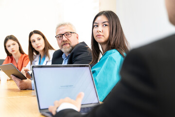 A group of people are sitting at a table with laptops and a projector. They are likely discussing a project or presentation