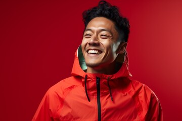 Obraz premium Portrait of a smiling asian man in his 30s wearing a functional windbreaker on solid color backdrop