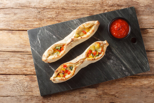 Delicious sorrentine alle verdure pizza with cheese and vegetables pepper, tomatoes, artichoke, zucchini cooked in a wood-fired oven close-up on a slate board on the table. Horizontal top view