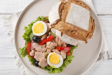 Tuna nicoise sandwich also known as pan bagnat closeup on the plate on the wooden table. Horizontal top view from above