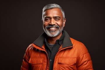 Obraz premium Portrait of a happy indian man in his 50s sporting a quilted insulated jacket isolated in solid color backdrop