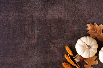 Fall corner border of white pumpkins with muted orange and brown autumn decor. Top view on a rustic dark stone background with copy space.