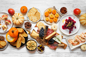 Autumn theme appetizer table scene against a white wood background. Charcuterie board, pumpkin and apple dips, crostini, cheeses and snacks. Above view.