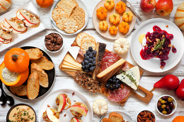 Autumn theme appetizer table scene against a white wood background. Charcuterie board, pumpkin and apple dips, crostini, cheeses and snacks. Top view.