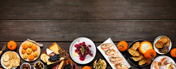 Autumn theme appetizer bottom border against a dark wood banner background. Charcuterie board, pumpkin and apple dips, crostini, cheeses and snacks. Top view.