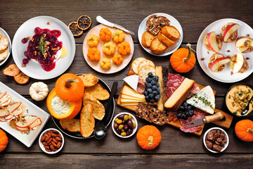 Fall theme appetizer table scene against a dark wood background. Charcuterie board, pumpkin and apple dips, crostini, cheeses and snacks. Top view.