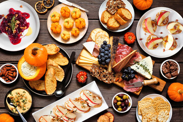 Fall theme appetizer table scene against a dark wood background. Charcuterie board, pumpkin and...