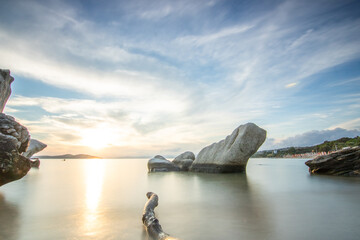 View through rocks on a sandy beach into the sunset. Landscape shot with a view to the horizon over...