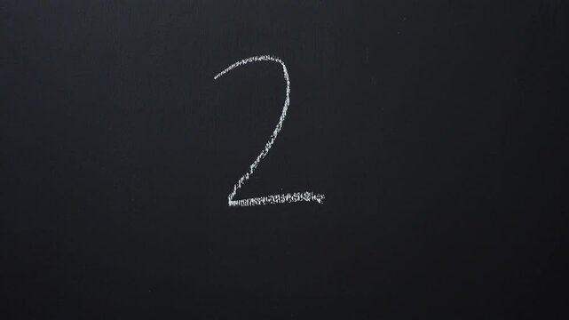 Hand writes the number 2 with white chalk on a black board