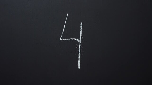 Hand writes the number 4 with white chalk on a black board
