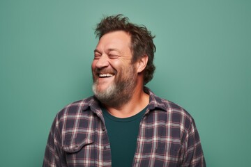 Portrait of a grinning man in his 40s wearing a comfy flannel shirt on solid pastel color wall