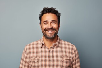 Portrait of a grinning man in his 40s wearing a comfy flannel shirt on solid pastel color wall