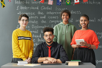 Portrait of male teacher smiling at camera posing together with diverse group of students during...