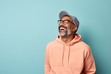 Portrait of a joyful indian man in his 50s sporting a comfortable hoodie while standing against solid pastel color wall