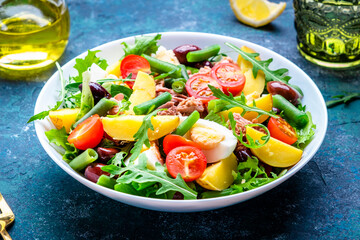 French gourmet salad with tuna, tomatoes, eggs, beans, potatoes and olives on blue background, top view