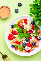 Fruit and berry salad with ricotta and honey, green background, top view