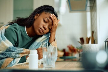 Ill African American woman holding her head in pain at home.