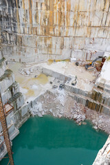 Machines working in the depths of a marble quarry in Vila Vi&ccedil;osa, Alentejo, Portugal. Industrial equipment extracting marble blocks amidst a rugged landscape of stone and dust.