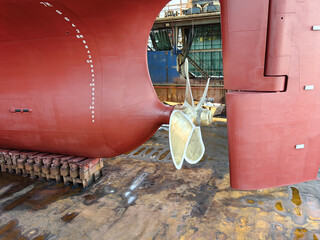 The rear end and propeller of a huge seagoing vessel in dry dock undergoing repairs