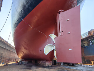 The rear end and propeller of a huge seagoing vessel in dry dock undergoing repairs