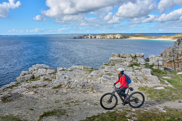 Fototapeta premium active senior woman cycling with her electric mountain bike along the wild coast of Finisterre in southern Brittany next to Camaret-sur-Mer, France
