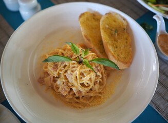 A plate of creamy pasta with basil, served alongside toasted garlic bread, set on a blue tablecloth in a casual dining setting.