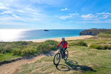 active senior woman cycling with her electric mountain bike along the  wild coast of Finisterre in...