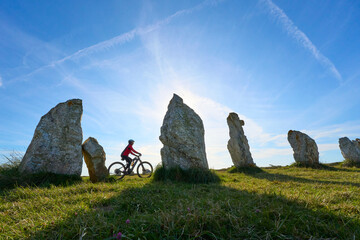 woman cycling between the neolithic menhirs of Camaret sur mer in Brittany, France