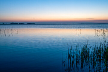Ruhiger See bei Sonnenuntergang mit Schilf und sanften Farben im Vordergrund
