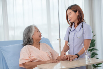 Fototapeta premium Asian female home nursing holding hand of older lady on the bed and encouraging patient