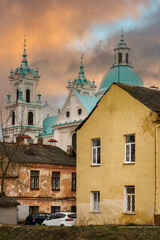 The urban landscape at sunset. A Catholic church against the background of old houses and orange clouds.