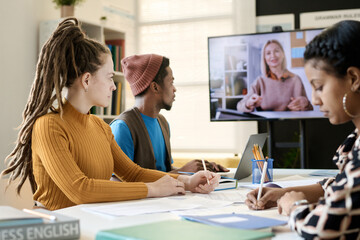 Diverse group of young people watching video lesson with young woman talking on TV screen